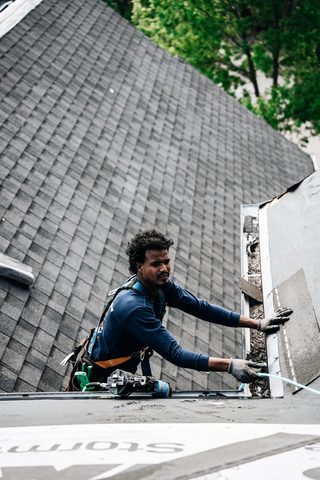 Roofer in a safety harness fitting shingles tight against a wall